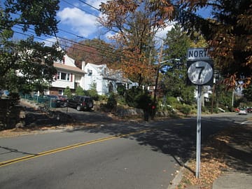 A quiet suburban street with autumn trees, houses, and a "Route 7 North" road sign in new jersey
